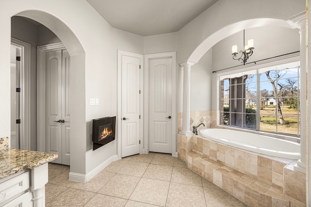 full bath with a garden tub, a glass covered fireplace, tile patterned flooring, and a chandelier