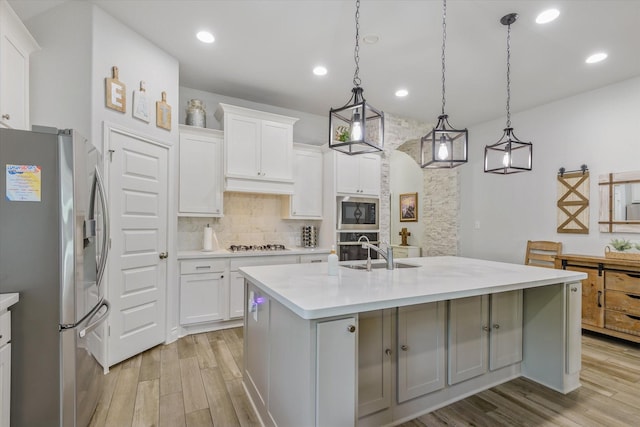 kitchen with appliances with stainless steel finishes, light wood-type flooring, a sink, decorative backsplash, and light countertops