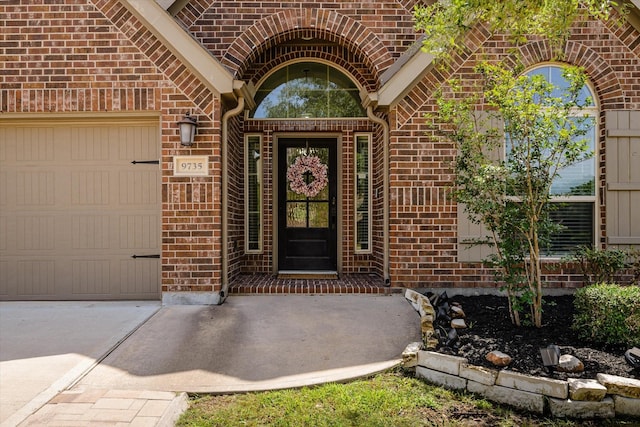 entrance to property featuring brick siding, an attached garage, and driveway