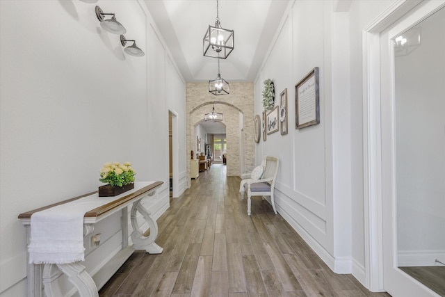 corridor featuring wood finished floors, arched walkways, and a chandelier