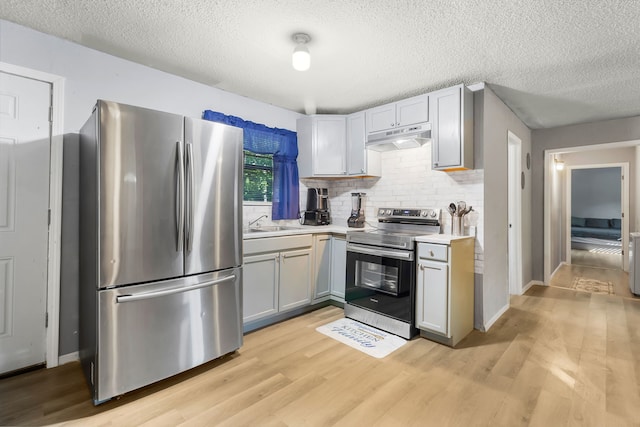 60 W Sierra Rd, Coldspring, TX 77331 - kitchen featuring appliances with stainless steel finishes, under cabinet range hood, light wood-type flooring, a textured ceiling, and light countertops