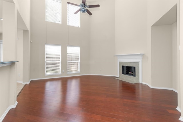 16503 Brightling Ln, Houston, TX 77090 - unfurnished living room featuring a ceiling fan, a high ceiling, hardwood / wood-style floors, a fireplace, and baseboards