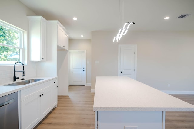6322 Sayers St, Houston, TX 77026 - kitchen featuring stainless steel dishwasher, a center island, light wood finished floors, white cabinetry, and hanging light fixtures