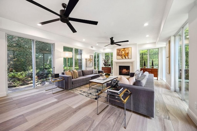 living area with a lit fireplace, a ceiling fan, plenty of natural light, wood finished floors, and recessed lighting