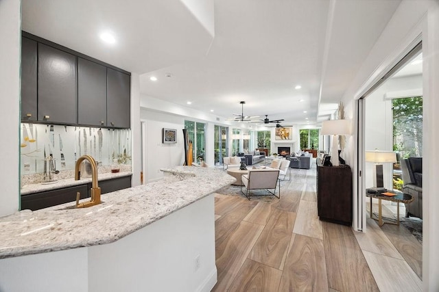 kitchen with a sink, a warm lit fireplace, light wood finished floors, recessed lighting, and light stone counters