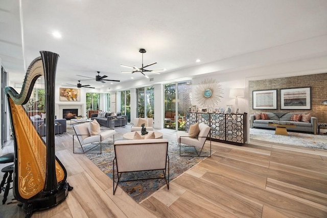 living area featuring a warm lit fireplace, recessed lighting, light wood-style flooring, and ceiling fan