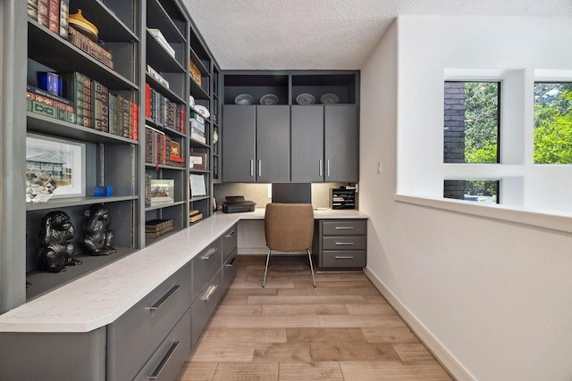 office space featuring built in desk, a textured ceiling, light wood-style floors, and baseboards