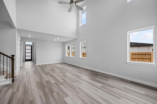 8802 Cecil Garden Ln, Cypress, TX 77433 - unfurnished living room featuring a towering ceiling, stairs, wood finished floors, baseboards, and a ceiling fan