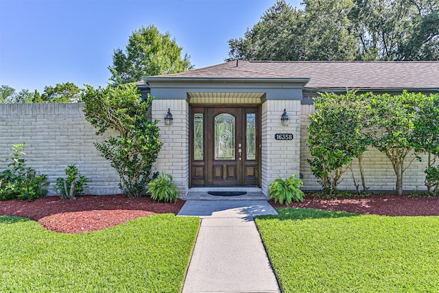 16358 Havenpark Dr, Houston, TX 77059 - view of exterior entry featuring brick siding, a yard, and a shingled roof