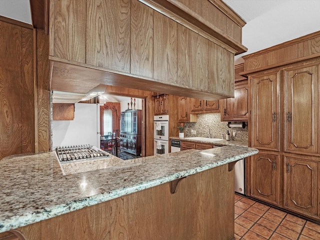 11821 15th St, Santa Fe, TX 77510 - kitchen with backsplash, a breakfast bar, brown cabinetry, light tile patterned flooring, and white appliances