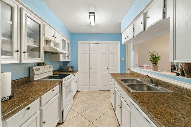 kitchen with white appliances, a sink, under cabinet range hood, dark countertops, and glass insert cabinets