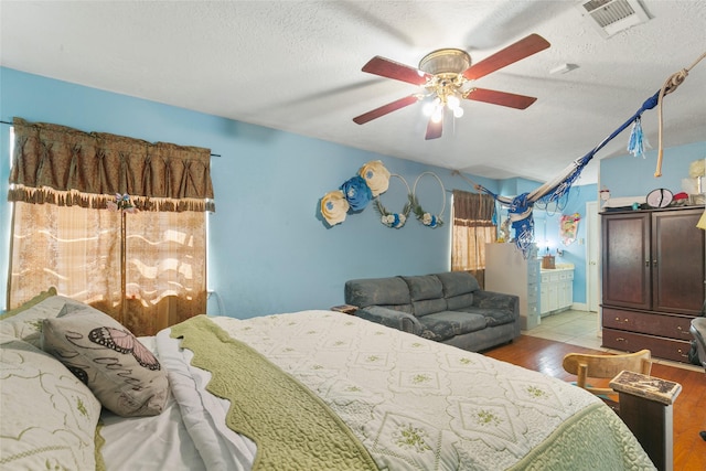 bedroom with wood finished floors, a textured ceiling, ceiling fan, and ensuite bath