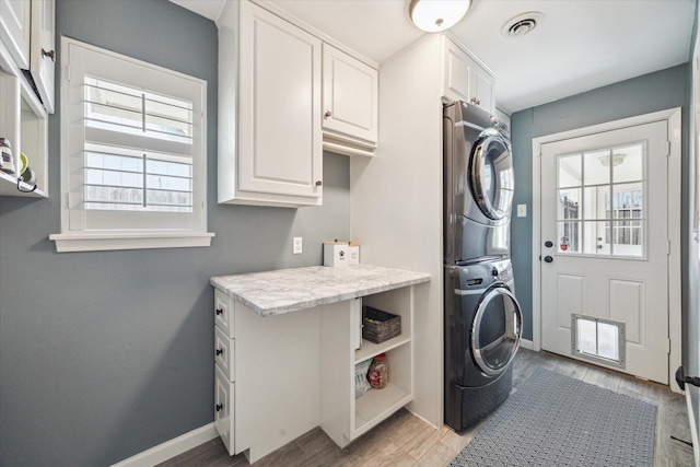 12310 Woodthorpe Ln, Houston, TX 77024 - laundry room featuring stacked washer and clothes dryer, cabinet space, light wood finished floors, and baseboards