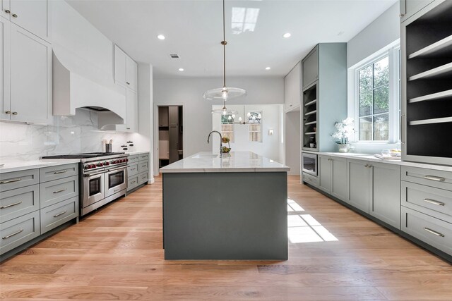 3314 La Salle St, Houston, TX 77027 - kitchen featuring appliances with stainless steel finishes, gray cabinets, an island with sink, light wood-style flooring, and light stone countertops