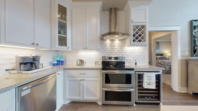 985 Sue Dr, Crystal Beach, TX 77650 - kitchen featuring appliances with stainless steel finishes, wall chimney exhaust hood, beverage cooler, white cabinetry, and wood finished floors