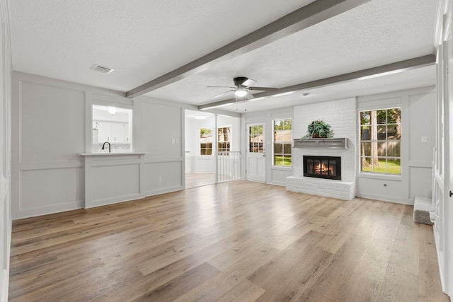 5310 Brownlee Ln, Spring, TX 77379 - unfurnished living room featuring beamed ceiling, light wood-style floors, a decorative wall, ceiling fan, and a fireplace