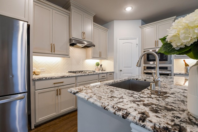 209 Cambria Green Ln, Katy, TX 77493 - kitchen featuring appliances with stainless steel finishes, under cabinet range hood, a sink, light stone countertops, and tasteful backsplash