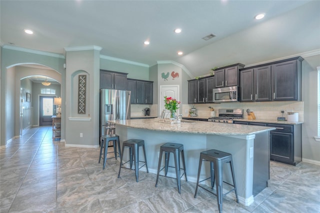 2255 Golden Laurel Dr, Conroe, TX 77304 - kitchen with appliances with stainless steel finishes, a breakfast bar area, decorative backsplash, arched walkways, and light stone counters
