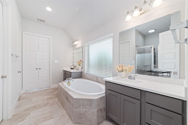 bathroom with a stall shower, a garden tub, two vanities, vaulted ceiling, and baseboards