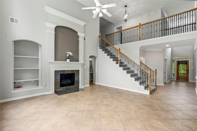 unfurnished living room featuring a ceiling fan, built in shelves, a high ceiling, light tile patterned floors, and a fireplace