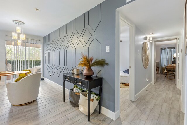 8051 Bay Branch Dr Unit 324, The Woodlands, TX 77382 - hallway featuring baseboards, a chandelier, light wood-style floors, and an accent wall