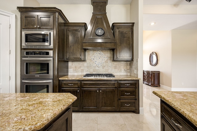 2119 Red Bird Ln, Brookshire, TX 77423 - kitchen featuring stainless steel appliances, premium range hood, backsplash, light stone countertops, and dark brown cabinetry