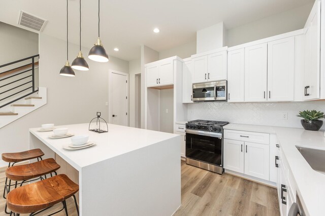 3312 Bremond St, Houston, TX 77004 - kitchen with stainless steel appliances, a kitchen breakfast bar, light wood-type flooring, tasteful backsplash, and white cabinets