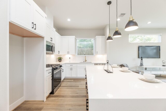 3312 Bremond St, Houston, TX 77004 - kitchen with stainless steel appliances, a sink, white cabinets, light wood-style floors, and a kitchen island