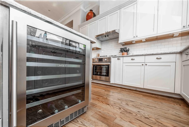 2110 Mason St, Houston, TX 77006 - kitchen featuring stainless steel oven, under cabinet range hood, wine cooler, tasteful backsplash, and crown molding