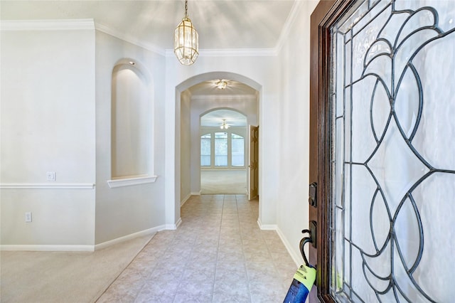 carpeted foyer featuring ornamental molding, arched walkways, and baseboards