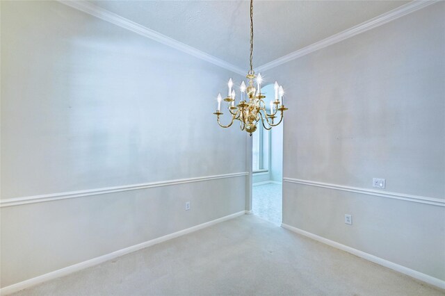 carpeted spare room with a chandelier, ornamental molding, and baseboards