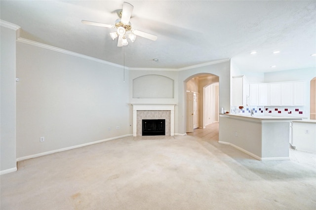 unfurnished living room featuring arched walkways, ceiling fan, light carpet, crown molding, and baseboards