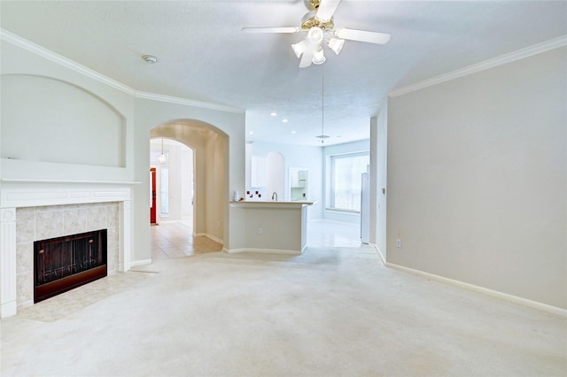 unfurnished living room with arched walkways, crown molding, ceiling fan, light colored carpet, and baseboards