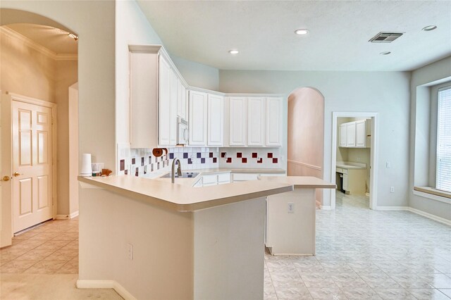 kitchen with white microwave, arched walkways, light countertops, white cabinets, and a peninsula