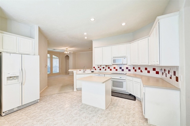 kitchen featuring white appliances, arched walkways, light countertops, a peninsula, and white cabinetry