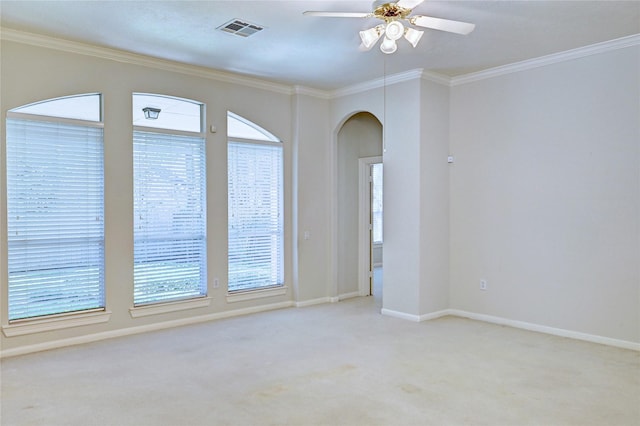 empty room featuring healthy amount of natural light, crown molding, arched walkways, light colored carpet, and a ceiling fan