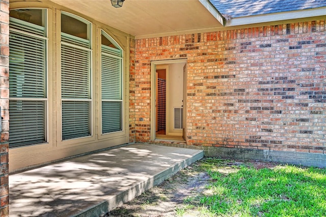 doorway to property with brick siding and a shingled roof