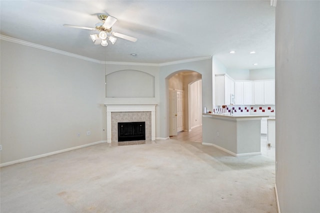 unfurnished living room featuring arched walkways, ceiling fan, light colored carpet, baseboards, and ornamental molding