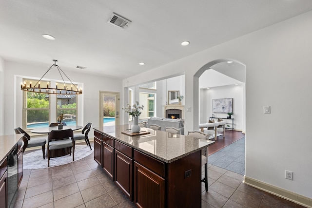 4603 Red Hawk Ct, Sugar Land, TX 77479 - kitchen featuring a kitchen bar, a chandelier, a lit fireplace, dark tile patterned flooring, and light stone countertops
