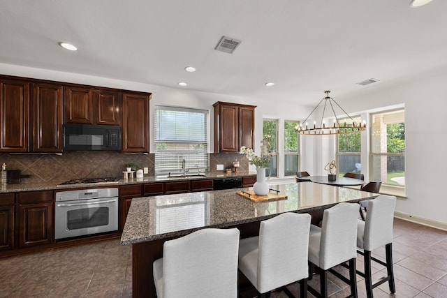 4603 Red Hawk Ct, Sugar Land, TX 77479 - kitchen with black appliances, a sink, a breakfast bar, decorative backsplash, and a chandelier