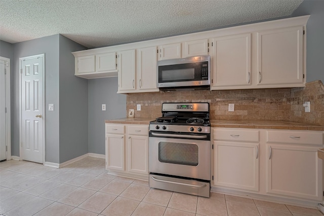 9911 Villa Verde Dr, Houston, TX 77064 - kitchen featuring appliances with stainless steel finishes, tile counters, light tile patterned flooring, tasteful backsplash, and white cabinets