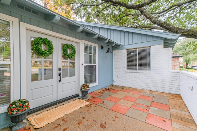 view of exterior entry featuring brick siding, board and batten siding, and a patio