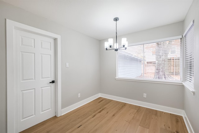 unfurnished dining area with a chandelier, baseboards, and light wood-style floors