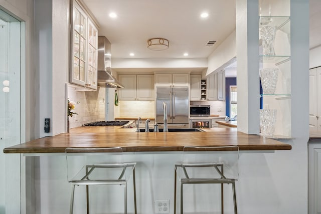 2618 Sunset Blvd, West University Place, TX 77005 - kitchen featuring wall chimney exhaust hood, appliances with stainless steel finishes, backsplash, glass insert cabinets, and a sink