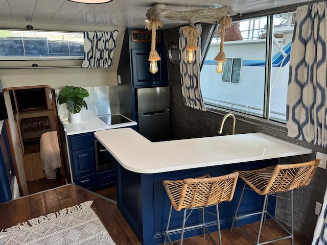 kitchen with stainless steel refrigerator, blue cabinets, dark wood-style floors, black electric cooktop, and a peninsula