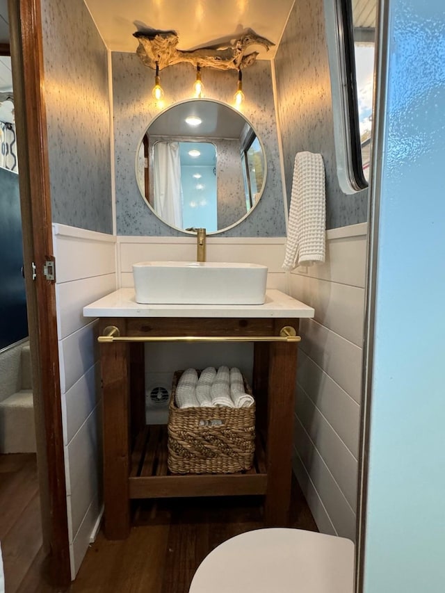 bathroom featuring a wainscoted wall, wallpapered walls, wood finished floors, vanity, and toilet