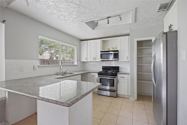 kitchen with stainless steel appliances, a sink, a peninsula, a textured ceiling, and open shelves