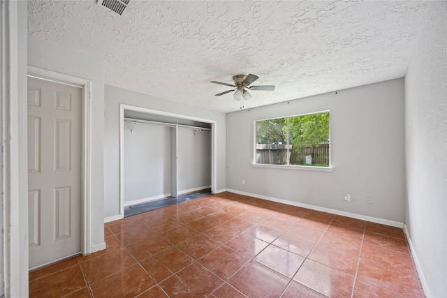 unfurnished bedroom featuring tile patterned flooring, a closet, a textured ceiling, baseboards, and a ceiling fan