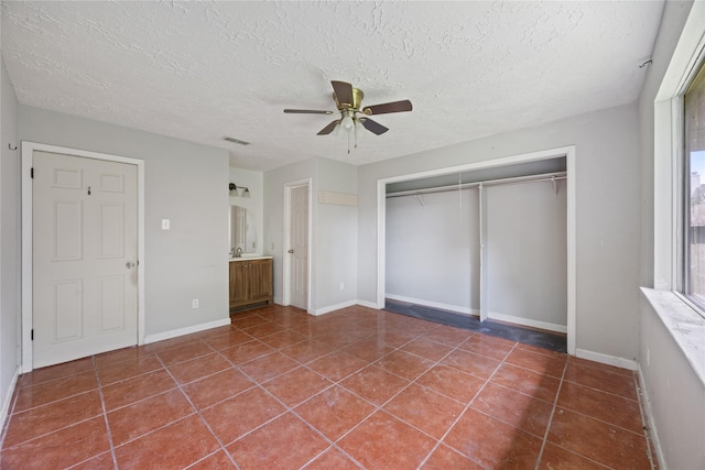 unfurnished bedroom with a closet, tile patterned floors, a textured ceiling, ceiling fan, and baseboards