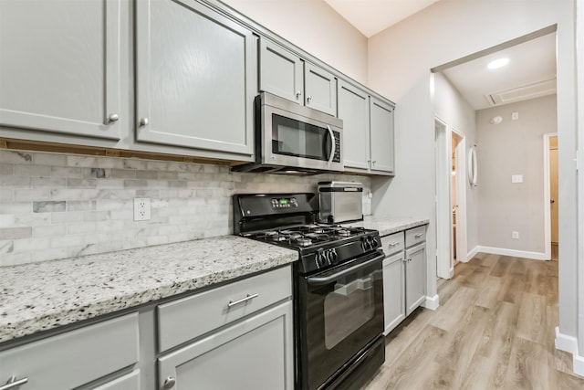 20810 Oak Rain Ct, Katy, TX 77449 - kitchen with stainless steel microwave, black range with gas stovetop, decorative backsplash, light wood finished floors, and gray cabinetry